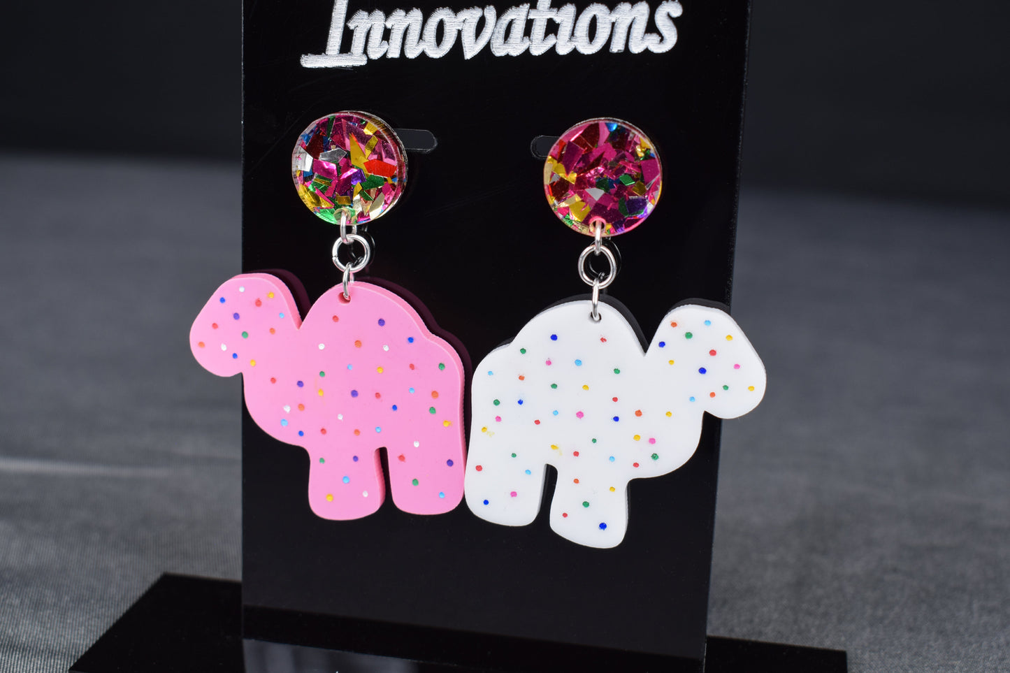 A pair of colorful acrylic earrings, featuring a camel shape with sprinkled dots and confetti accents