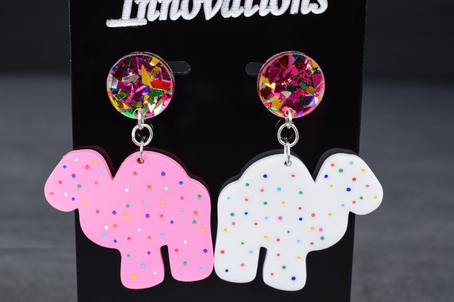 A pair of colorful acrylic earrings, featuring a camel shape with sprinkled dots and confetti accents