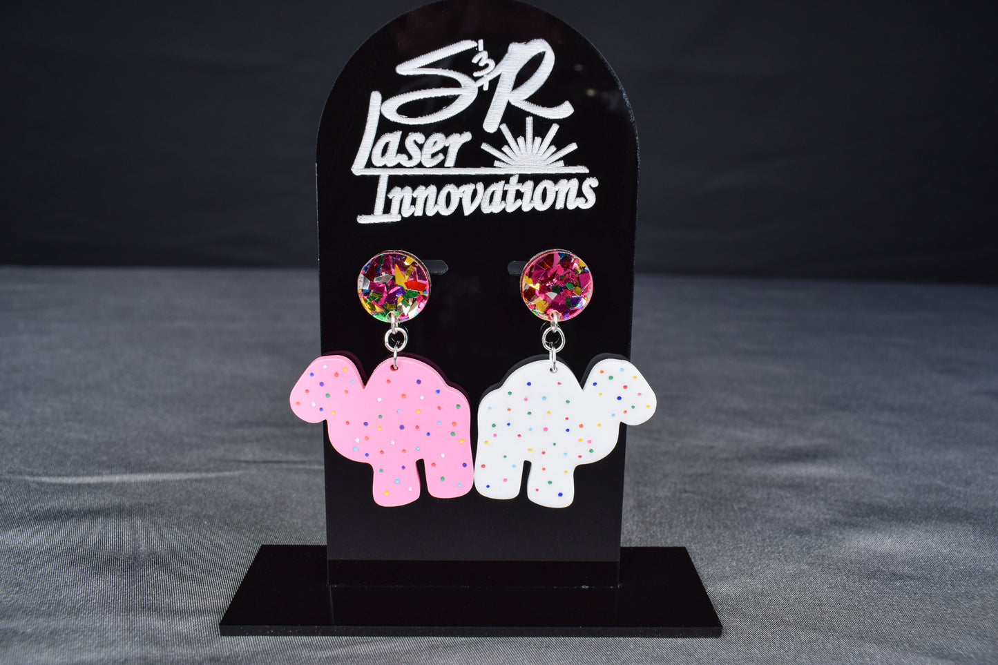 A pair of colorful acrylic earrings, featuring a camel shape with sprinkled dots and confetti accents