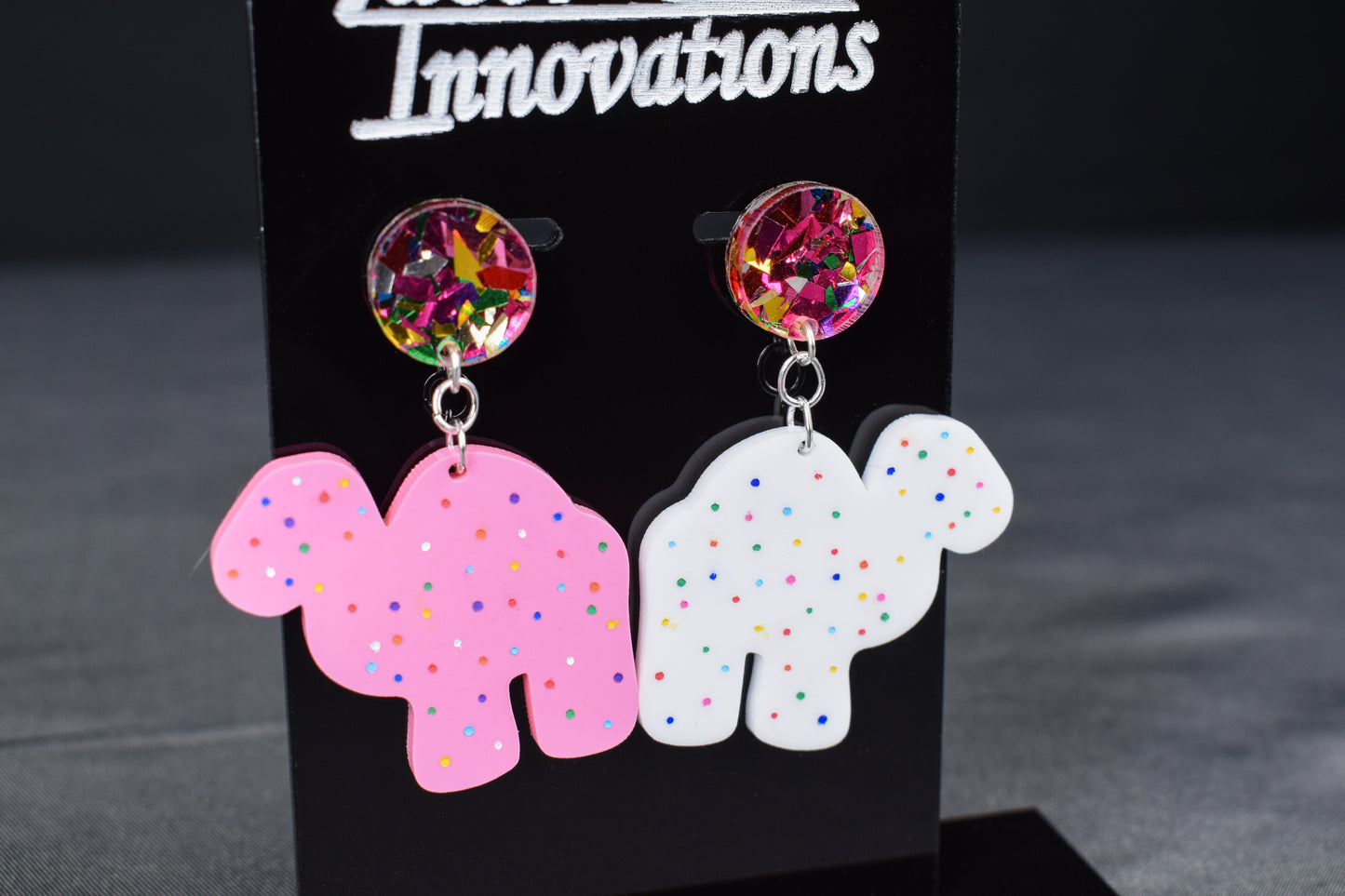 A pair of colorful acrylic earrings, featuring a camel shape with sprinkled dots and confetti accents
