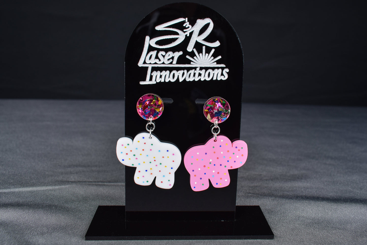 A pair of colorful acrylic earrings, featuring an elephant shape with sprinkled dots and confetti accents
