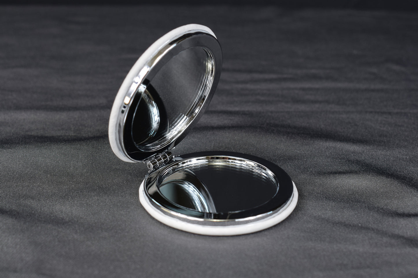 a compact mirror with a white leatherette cover partially opened to show the mirrors inside