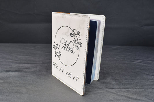 a laser engraved passport holder with a white marble leatherette cover, partially open to show a passport, against a gray background