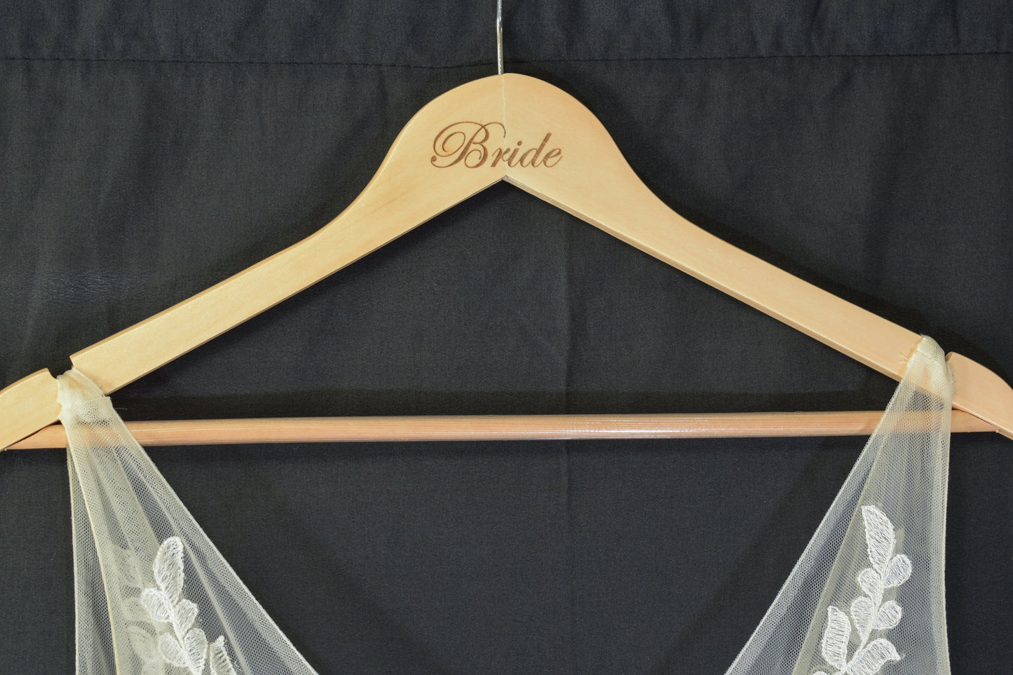 a wooden hanger with 'bride' laser engraved on it, holding up a floral design dress against a black background