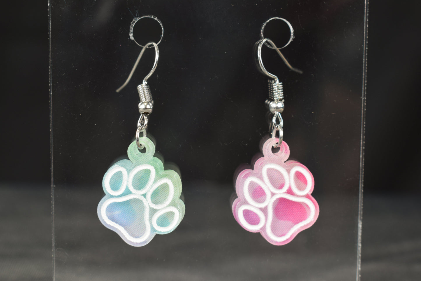 A pair of colorful acrylic earrings, featuring a paw print design, in rainbow leopard print with hypoallergenic earring hooks.