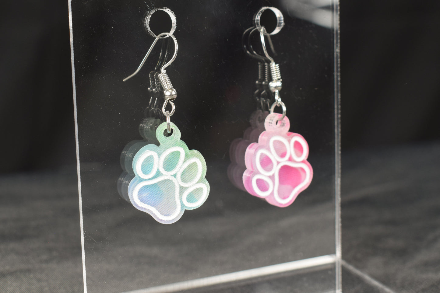 A pair of colorful acrylic earrings, featuring a paw print design, in rainbow leopard print with hypoallergenic earring hooks.