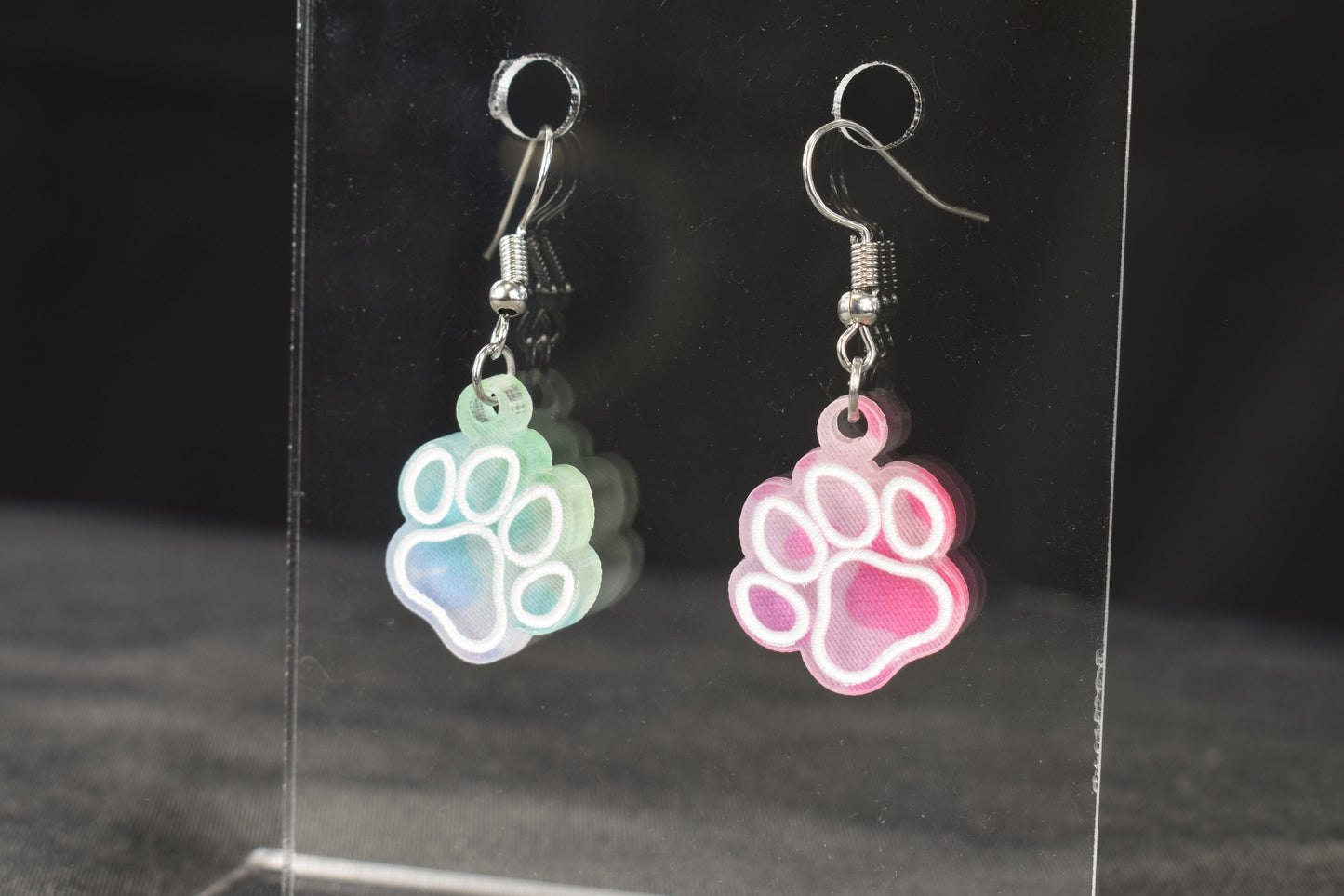A pair of colorful acrylic earrings, featuring a paw print design, in rainbow leopard print with hypoallergenic earring hooks.