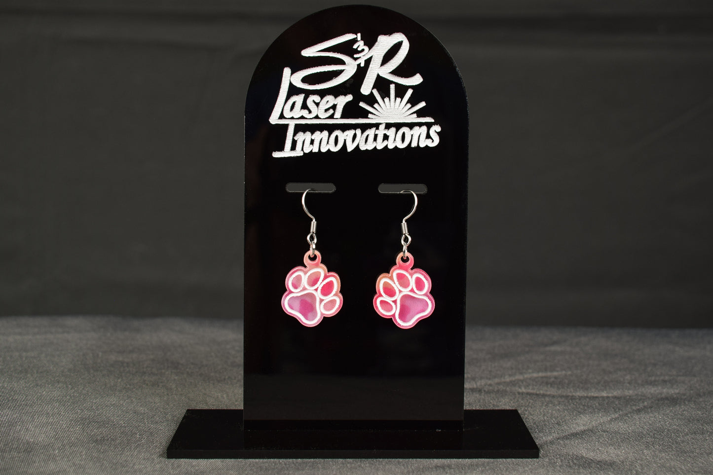 colorful acrylic paw print earrings with a bright hue, displayed on a black stand featuring the 'S&R Laser Innovations' logo