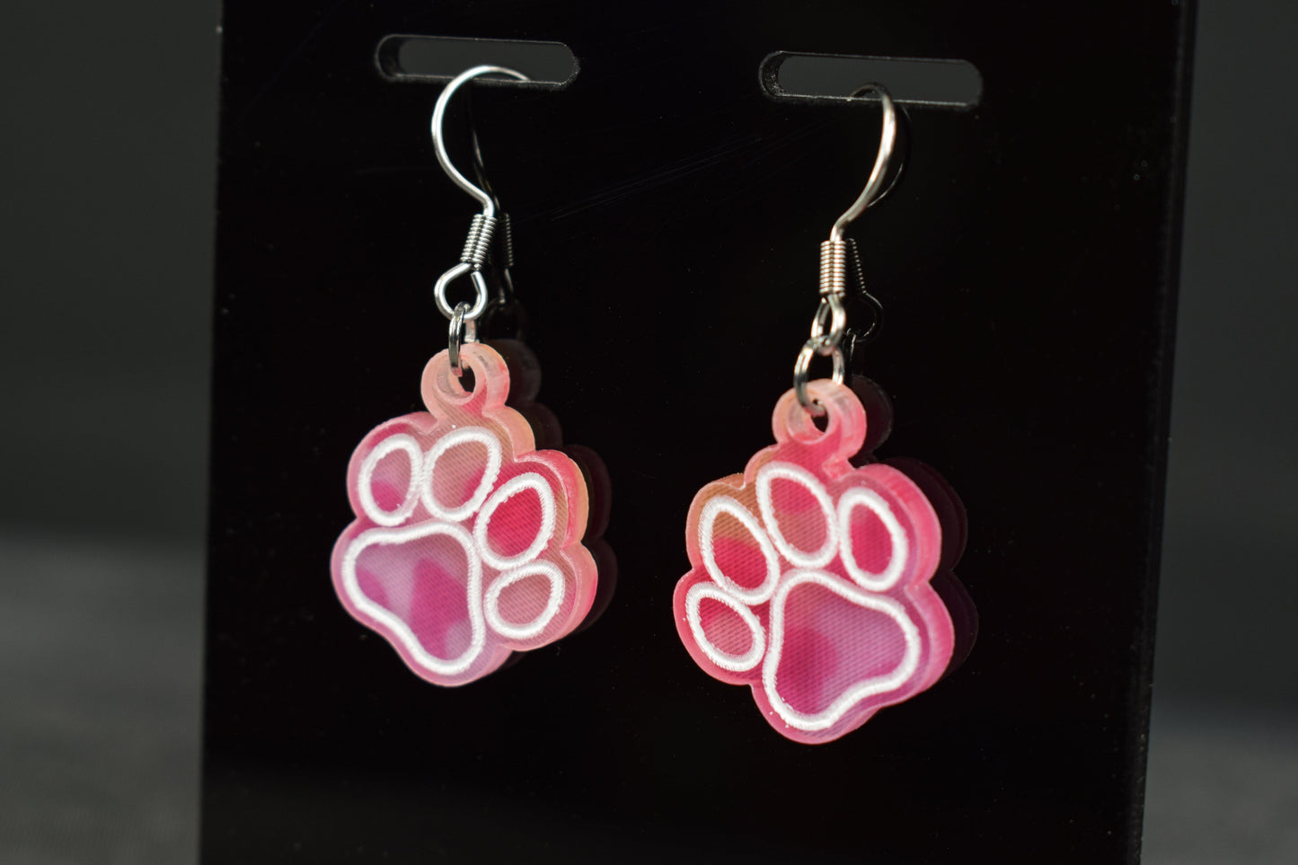 colorful acrylic paw print earrings with a bright hue, displayed on a black stand