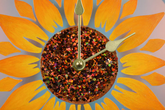 A close up view of the center of a hand painted sunflower clock, showcasing the glitter accents and gold colored hands