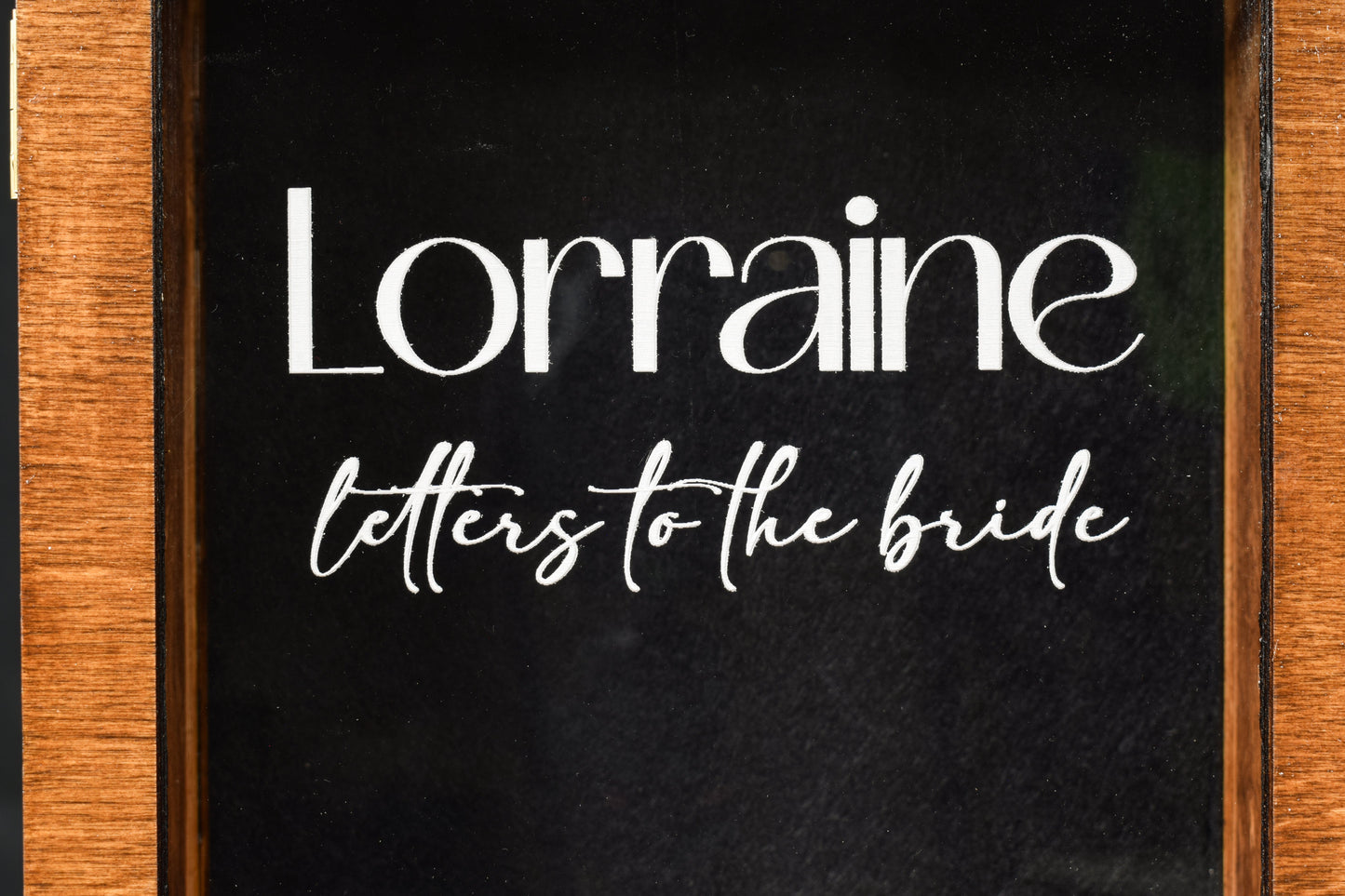 A close up view of a letter box, showcasing the clear lid with the engraving 'Lorraine letters to the bride' inside a wood border