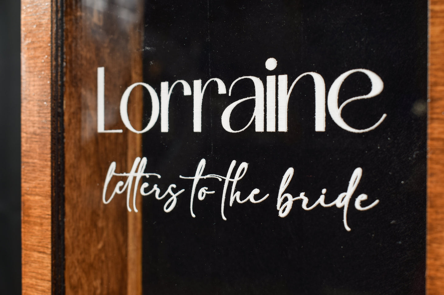 A side view of a handcrafted wooden letter box, showcasing the clear lid with the engraving 'Lorraine letters to the bride' in white