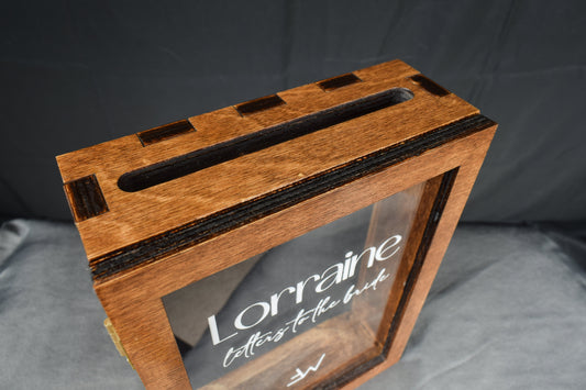 A handcrafted wooden letter box, showcasing the slot in the top for inserting letters and the clear lid with a custom engraving, set against a dark background