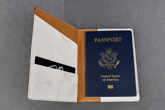 A synthetic leatherette passport holder in white marble color, open, displaying a simulated passport, with a card slot on the left side.