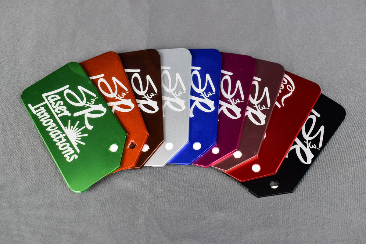 A collection of custom engraved aluminum luggage tags in various colors, each featuring a silver/gray engraved logo