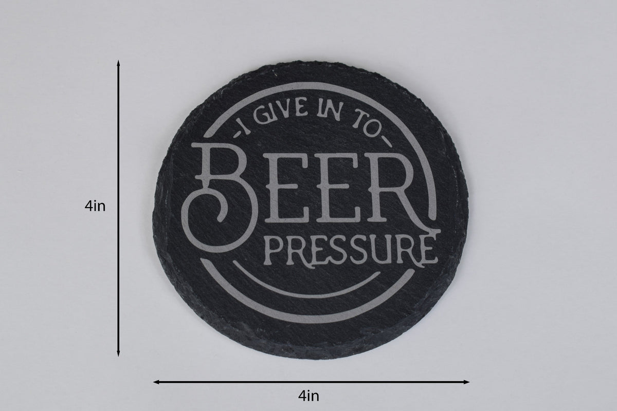 a round slate coaster with 'I give in to Beer Pressure' laser engraved in the center, placed on a white background with size markers