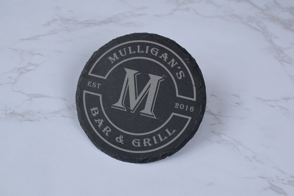 Black coaster with 'Mulligan's Bar & Grill' branding on a marble surface