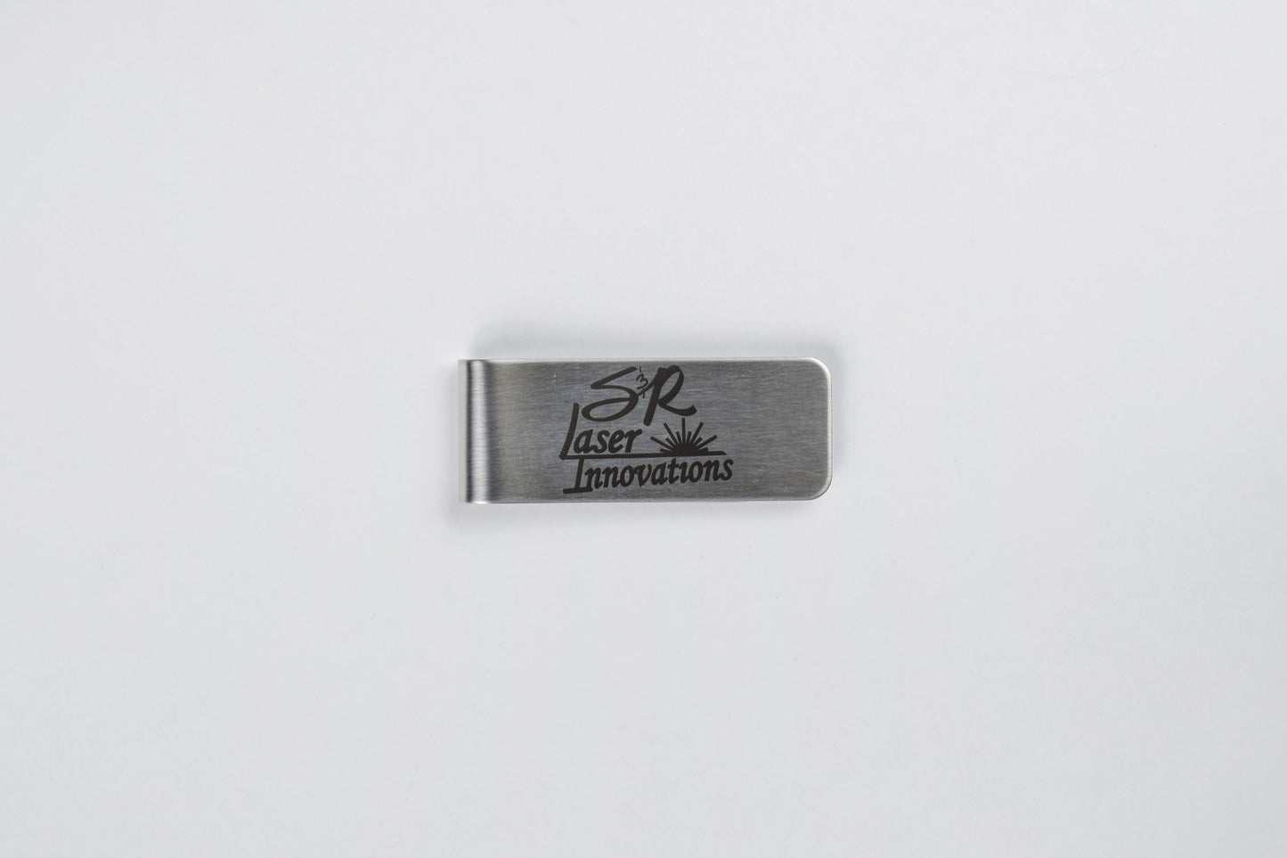 A stainless steel money clip with custom logo engraving, laid out on a white background.