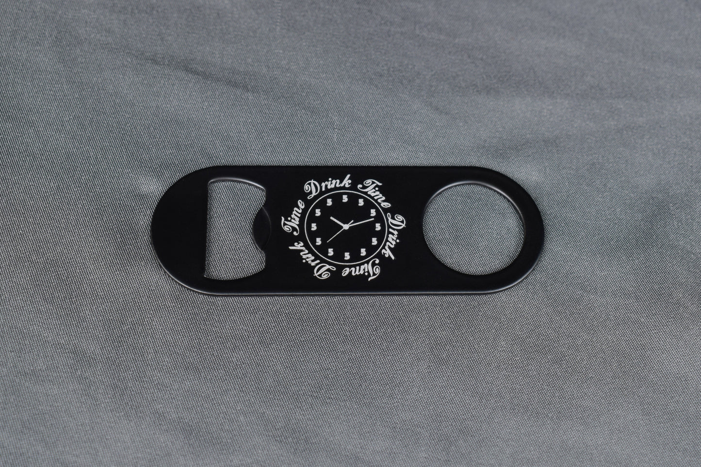 Black bottle opener with novelty clock design on gray fabric background