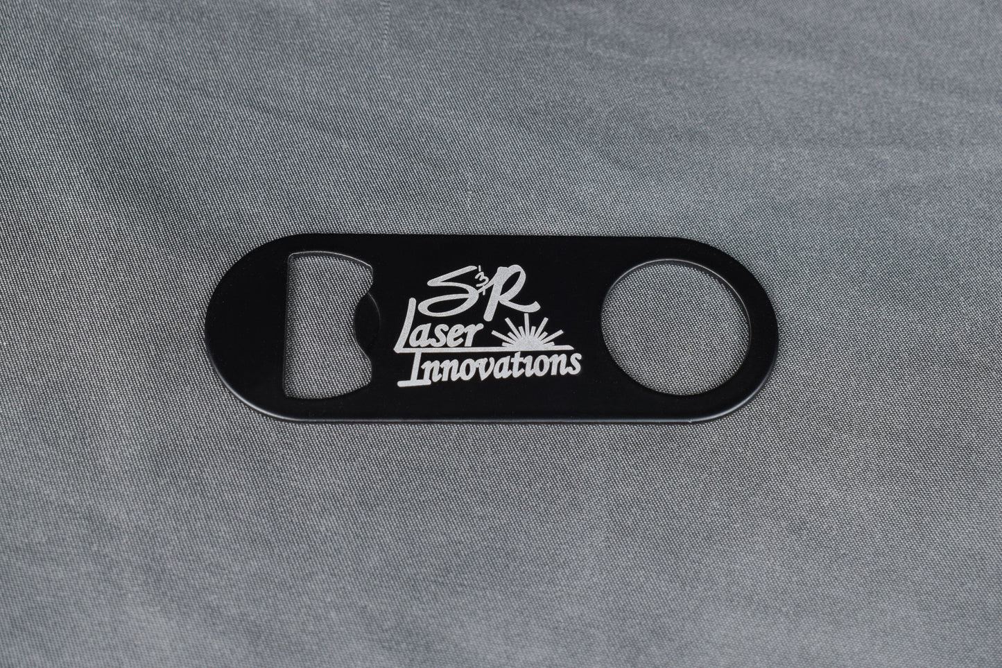 Black bottle opener with white logo on gray background