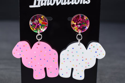 A pair of colorful acrylic earrings, featuring a camel shape with sprinkled dots and confetti accents