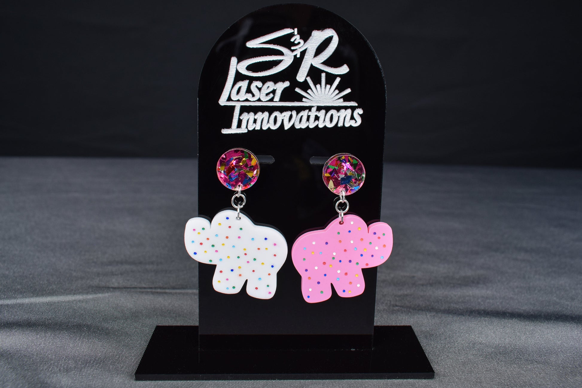 A pair of colorful acrylic earrings, featuring an elephant shape with sprinkled dots and confetti accents