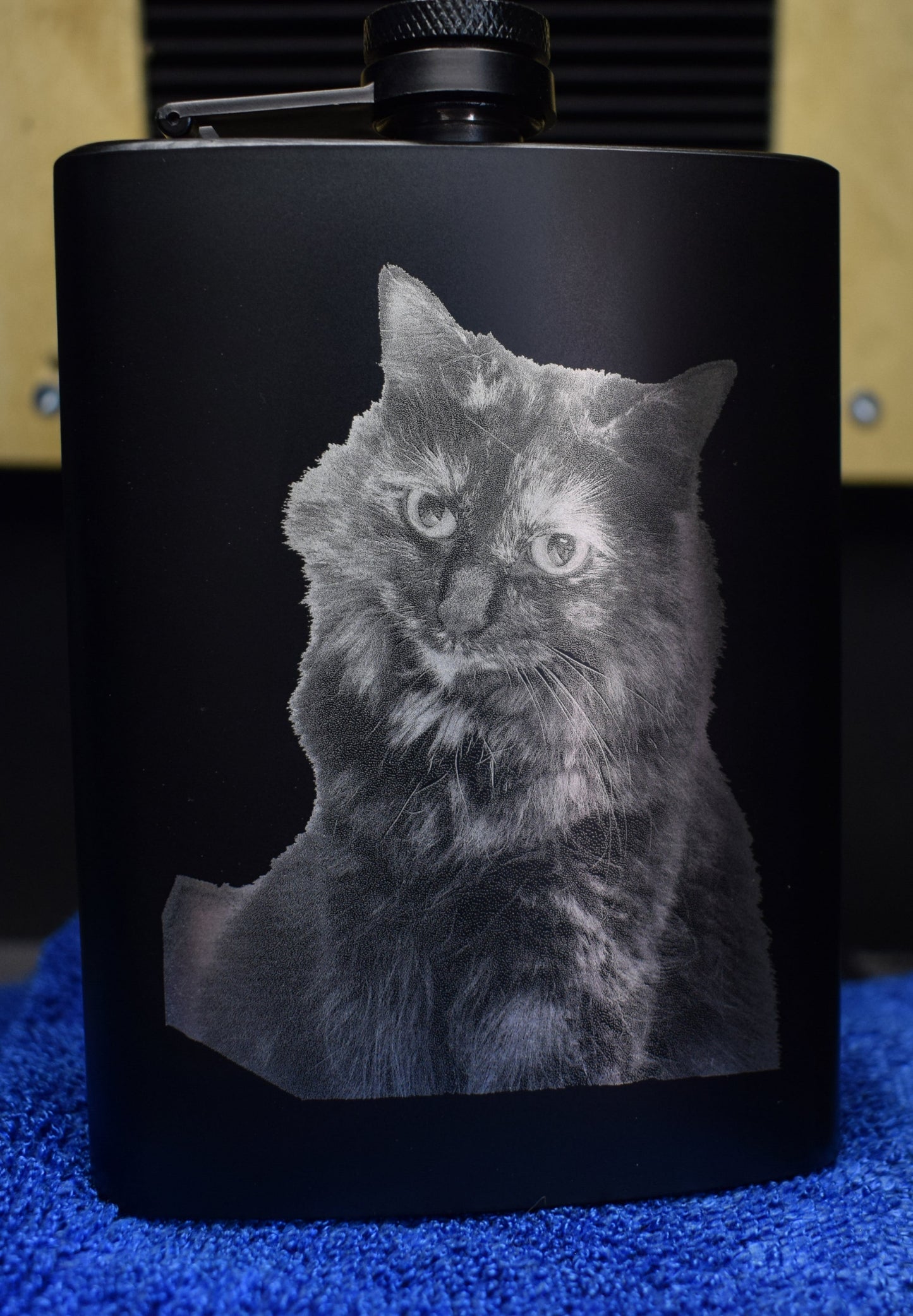 A black metal flask with a custom laser engraving of a cat's face.