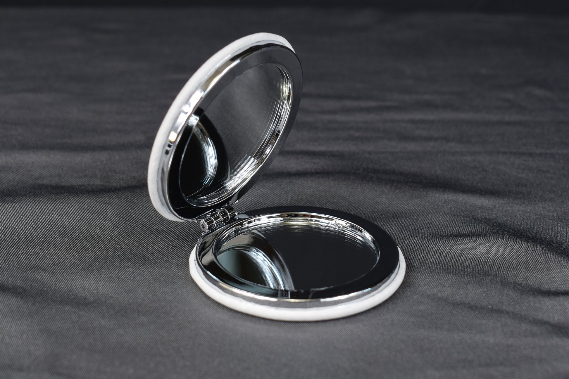 a compact mirror with a white leatherette cover partially opened to show the mirrors inside