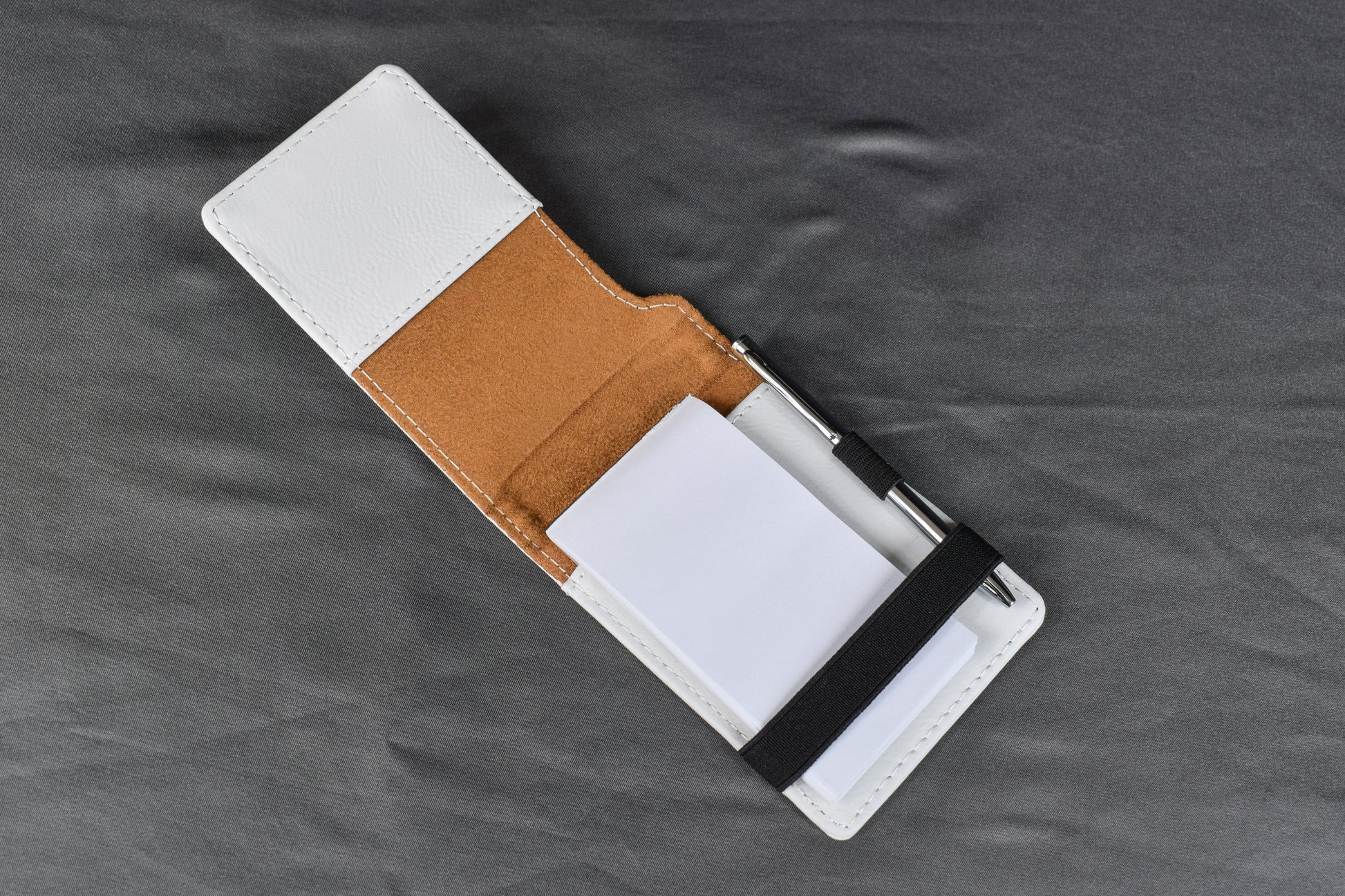 a white mini notebook opened to display the pen and paper inside, laying on a gray surface