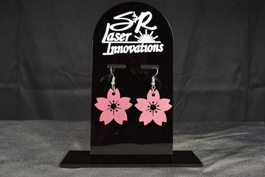 A pair of mauve metallic cherry blossom earrings displayed on a black stand with the brand name 'SR Laser Innovations' above.