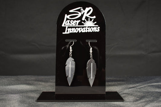 A pair of charcoal metallic acrylic feather earrings displayed on a black stand with 'SR Laser Innovations' branding above.