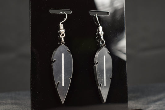 A close up view of a pair of charcoal metallic acrylic feather earrings displayed on a black stand, showcasing the silver hooks and white accent stripe