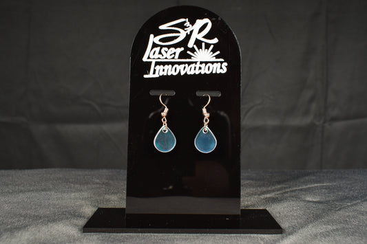 A pair of iridescent rainbow teardrop earrings displayed on a black stand with the brand name 'SR Laser Innovations' above.