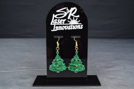 A pair of three-tiered Christmas tree earrings made of dark green swirl acrylic, displayed on a black stand with 'SR Laser Innovations' branding.