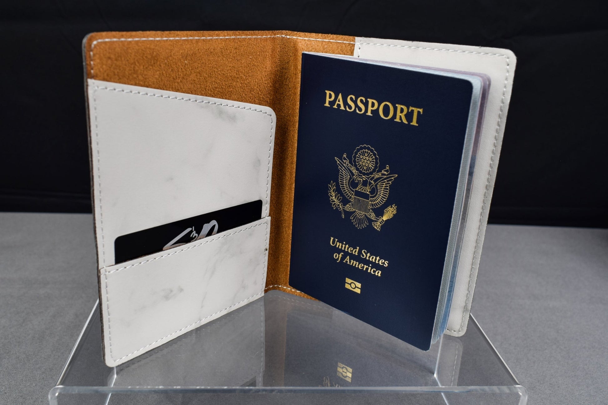 A synthetic leatherette passport holder in white marble color, open, displaying a simulated passport, with a card slot on the left side.