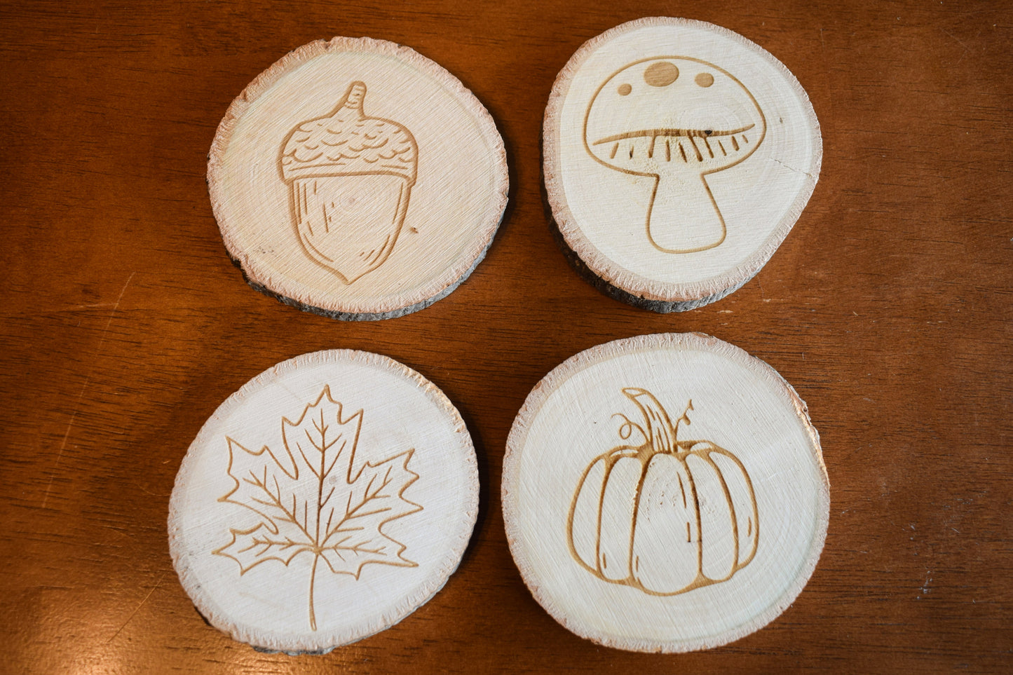 a set of four circular basswood coasters with fall themed designs laser engraved onto the surface