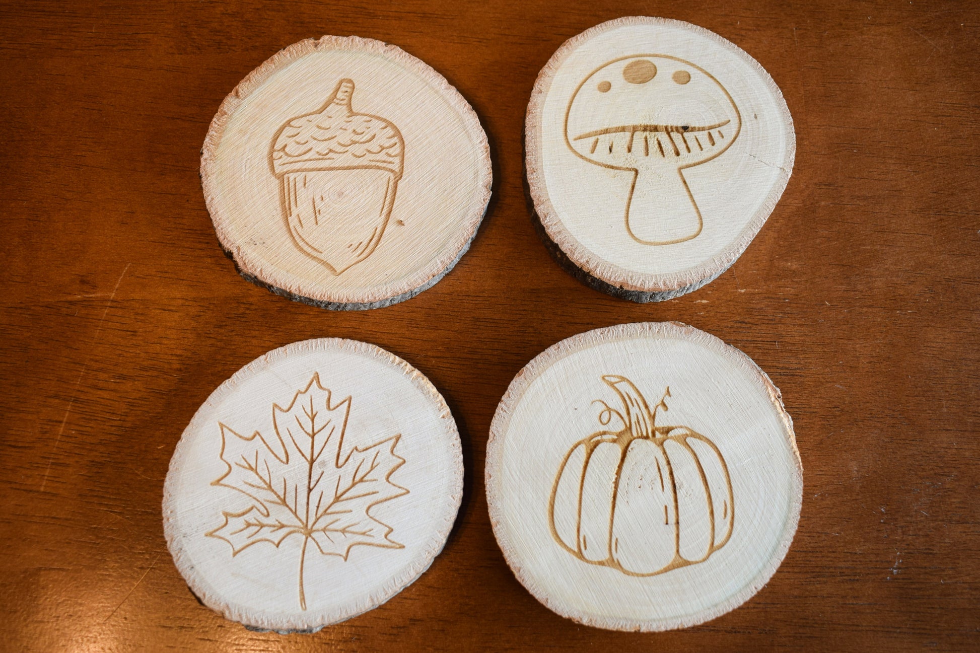 a set of four circular basswood coasters with fall themed designs laser engraved onto the surface