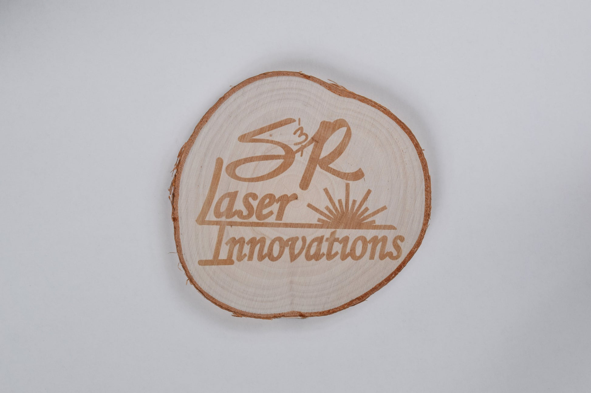 a birch coaster with S&R laser innovations logo engraved on it, against a white background