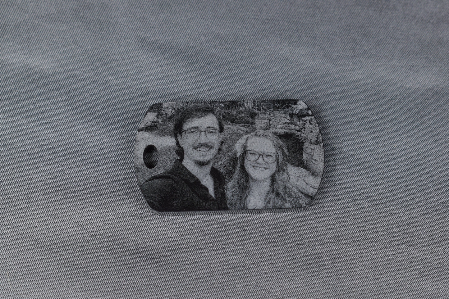 a black acrylic dogtag shaped keychain with a laser engraved image of a man and a woman standing in a garden