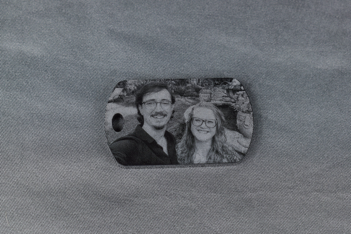 a black acrylic dogtag shaped keychain with a laser engraved image of a man and a woman standing in a garden