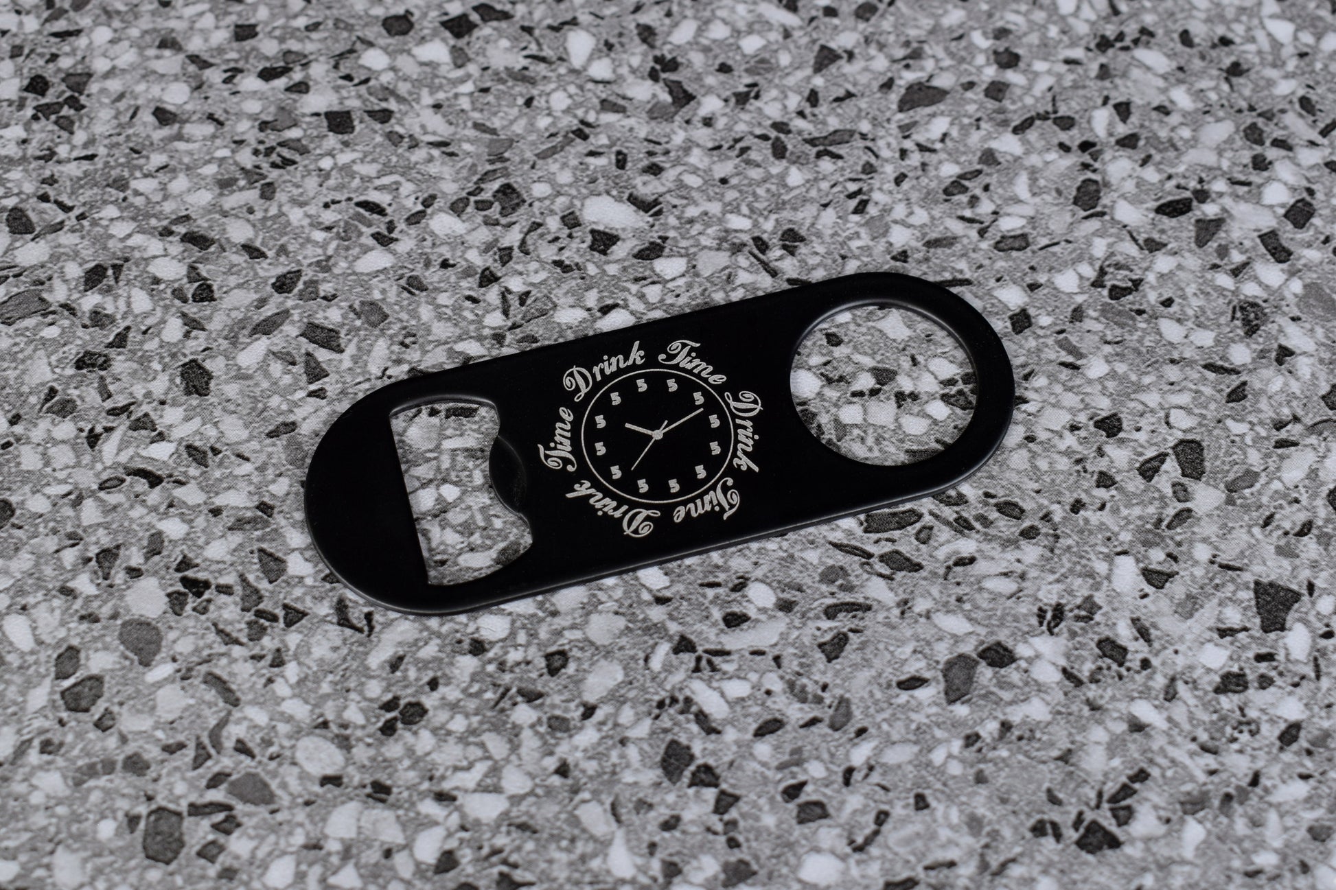 Black bottle opener with text on a textured gray surface