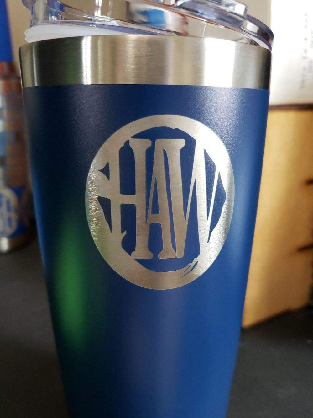 Blue tumbler with 'HAW' monogram on a blurred background
