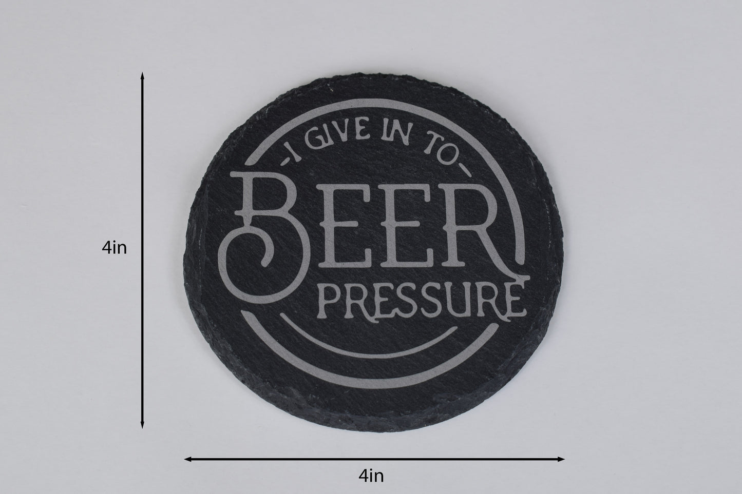 a round slate coaster with 'I give in to Beer Pressure' laser engraved in the center, placed on a white background with size markers