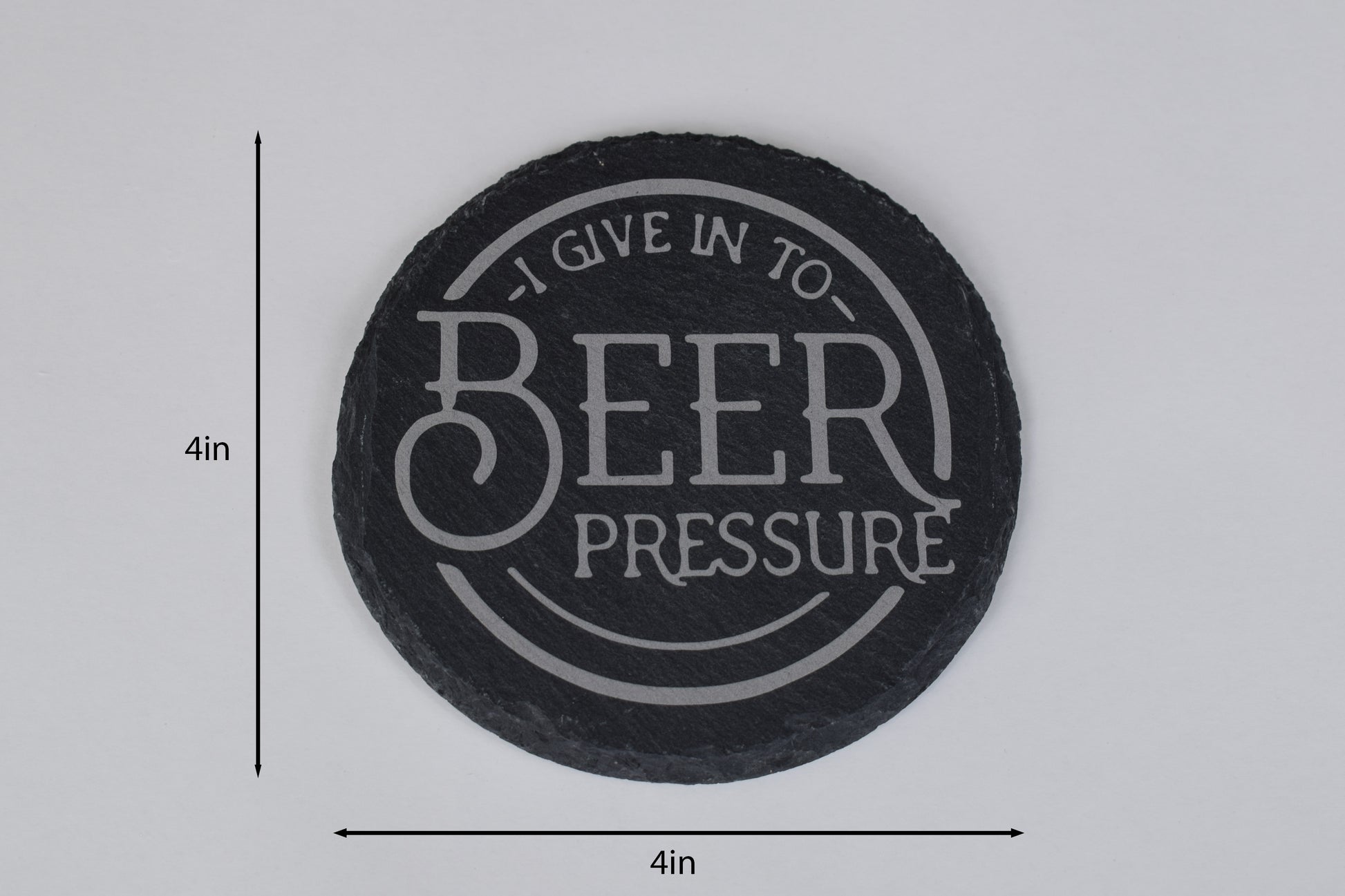 a round slate coaster with 'I give in to Beer Pressure' laser engraved in the center, placed on a white background with size markers