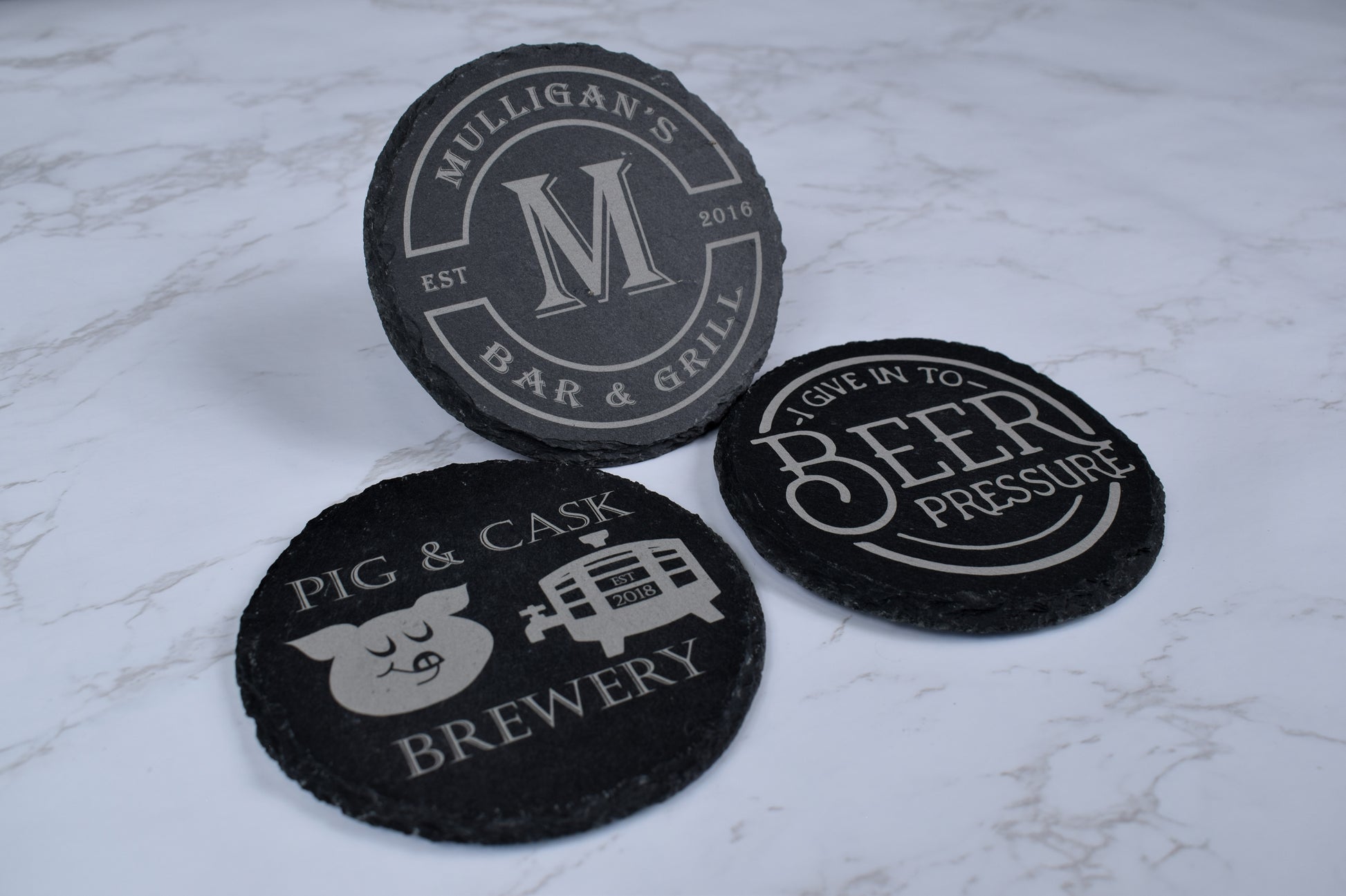 Three black coasters with white text and graphics on a light gray marble surface