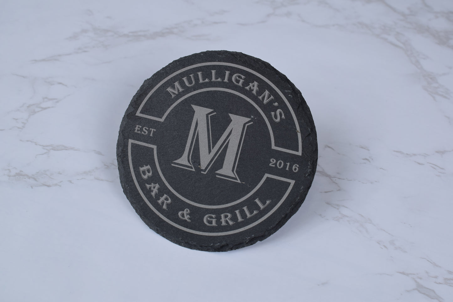 Black coaster with 'Mulligan's Bar & Grill' branding on a marble surface