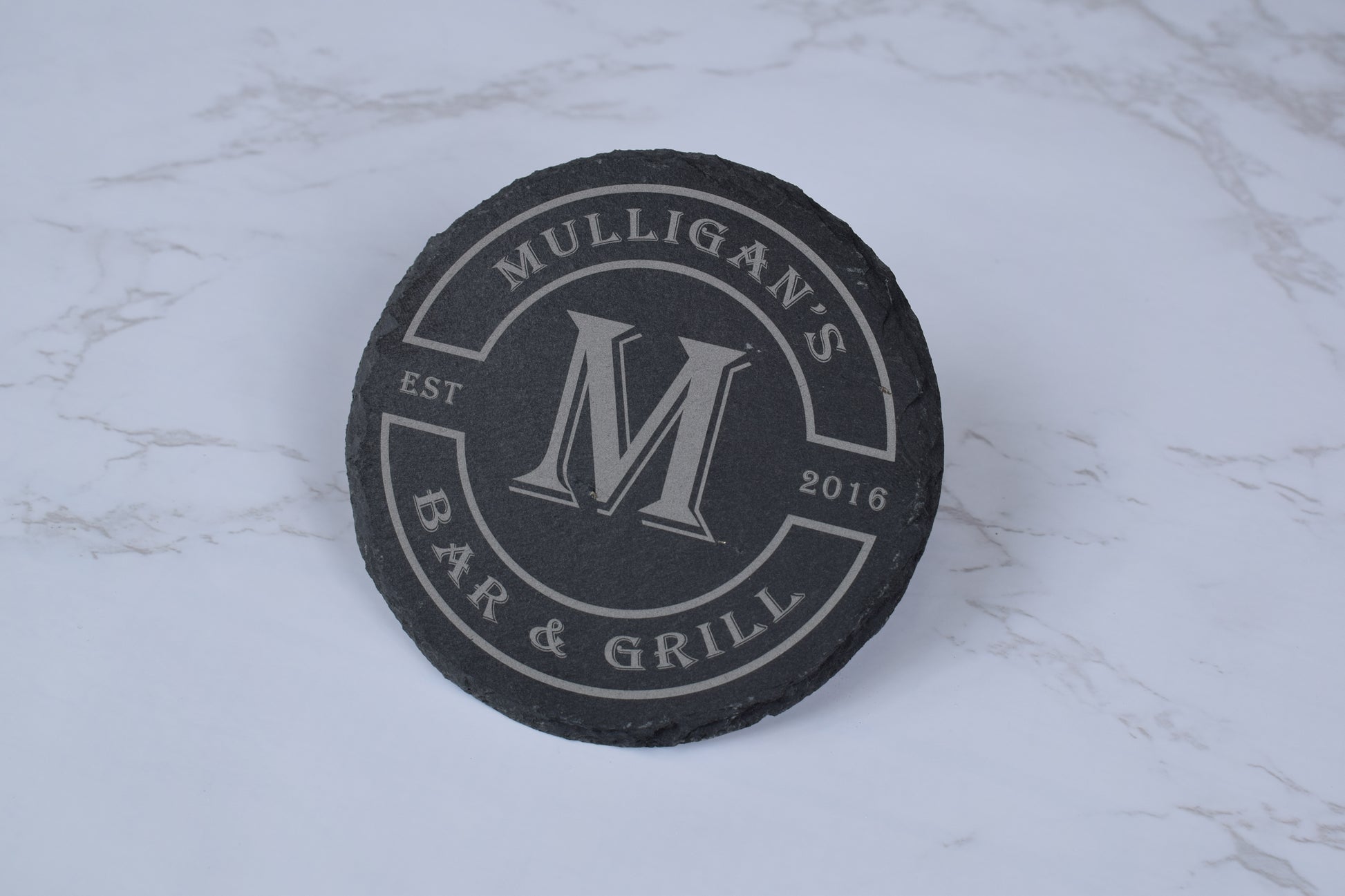 Black coaster with 'Mulligan's Bar & Grill' branding on a marble surface