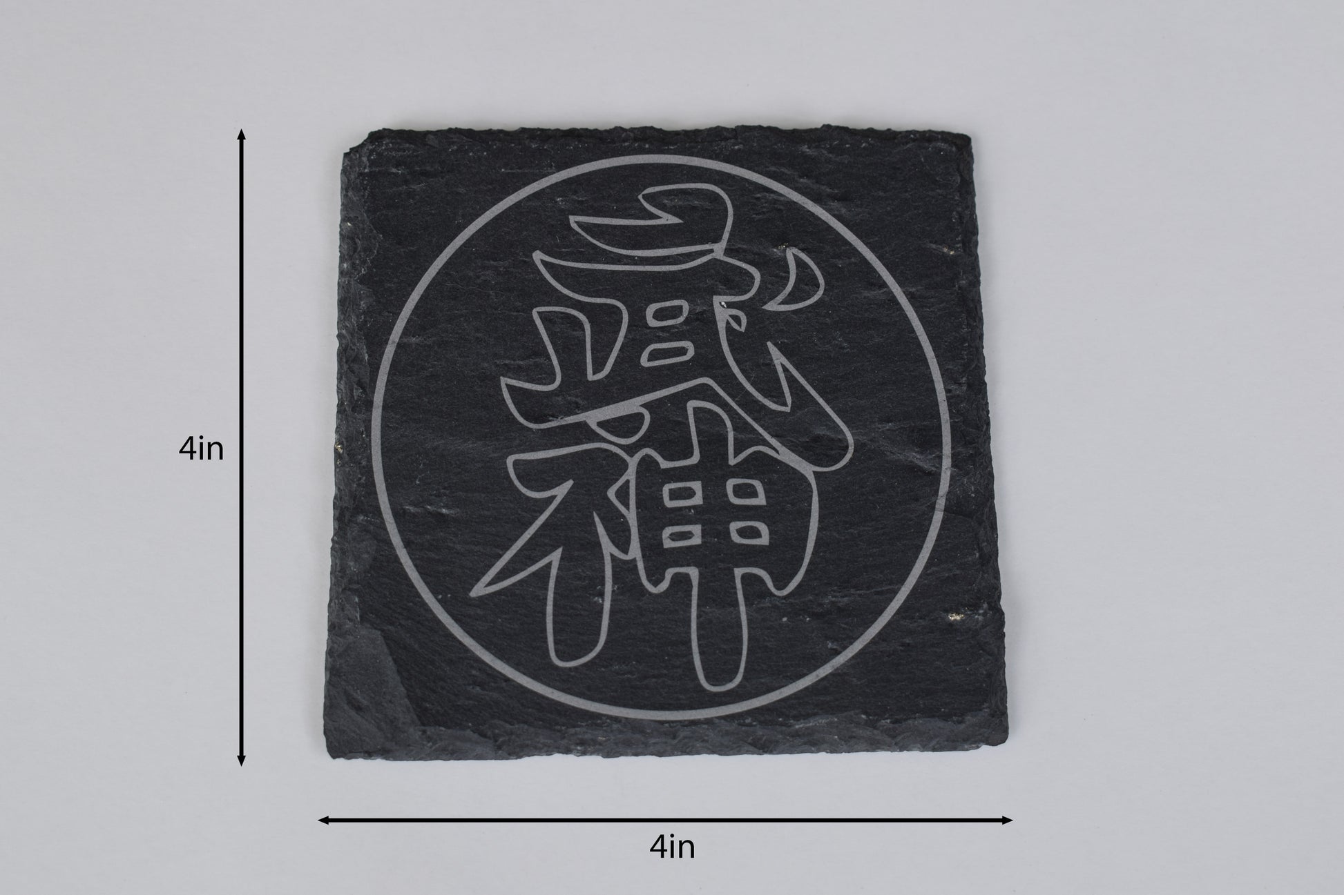 a square coaster made of black slate with a japanese symbol laser engraved in the center, placed on a white background with size markers