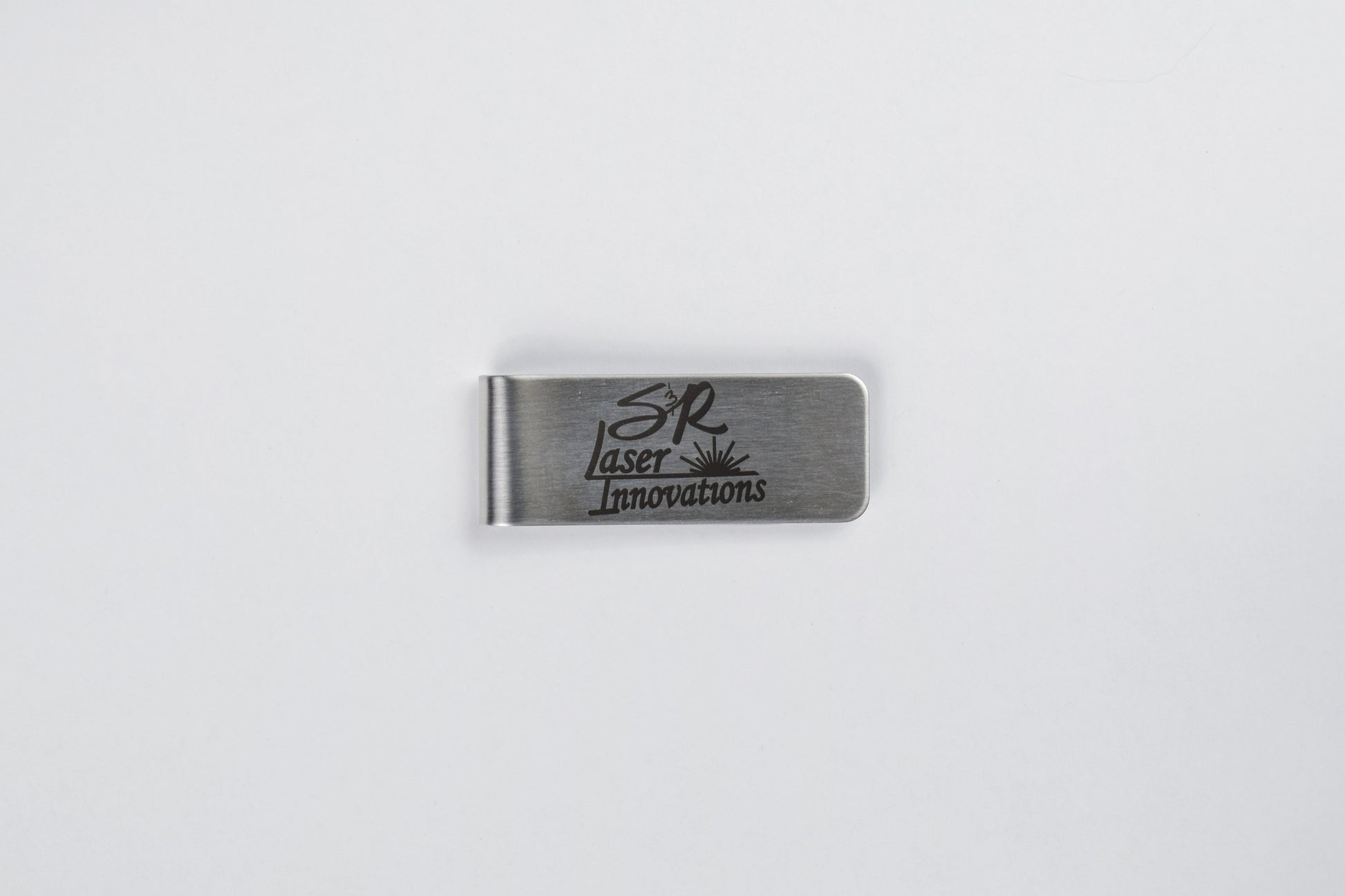 A stainless steel money clip with custom logo engraving, laid out on a white background.