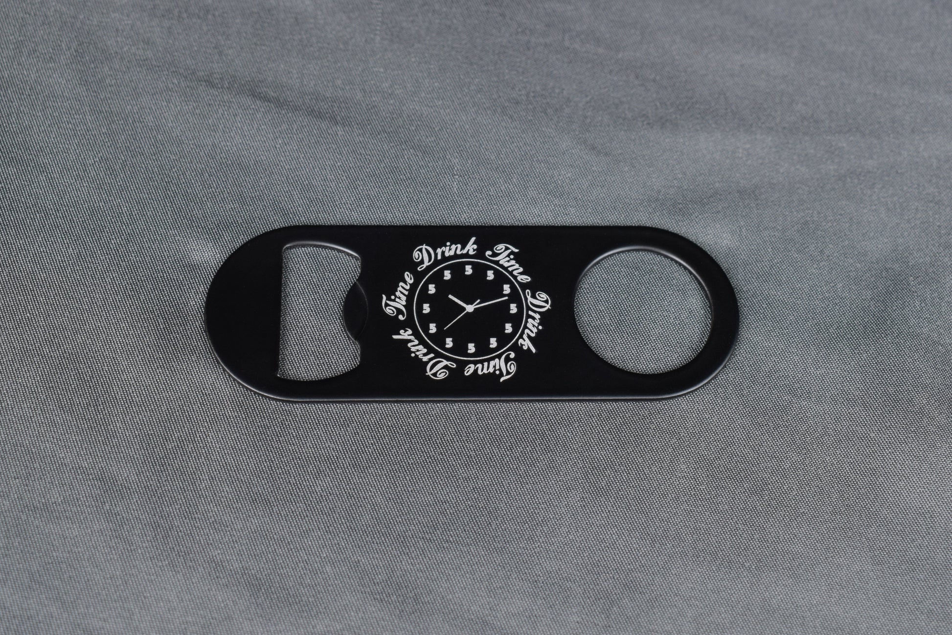 Black bottle opener with novelty clock design on gray fabric background